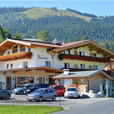 Ein charmantes Hotel mit blühenden Fensterkästen in einer landschaftlich reizvollen Umgebung. Im Hintergrund sind sanfte Berge zu sehen.