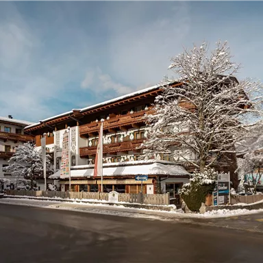 Ein malerisches Gebäude im winterlichen Ambiente mit Schnee bedeckten Bäumen. Im Hintergrund sind die Berge und ein klarer Himmel zu sehen.