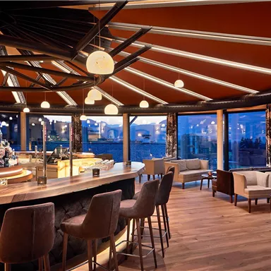 A stylish bar with round wooden details and large windows that create a cozy atmosphere. The space is modernly furnished and well-lit.