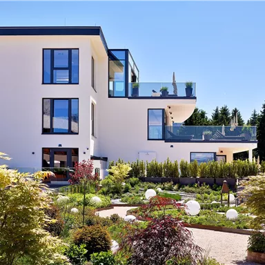 A modern, elegant house with large windows and a well-maintained garden. The surroundings are lush and inviting, perfect for a relaxing stay.