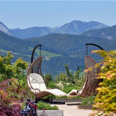 A beautiful view with two cozy hanging chairs in a garden. In the background, green hills and mountains can be seen.