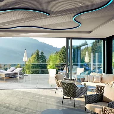 A modern living room with large windows offering a view of the mountains. Stylish furniture and a bright, inviting atmosphere create a cozy ambiance.