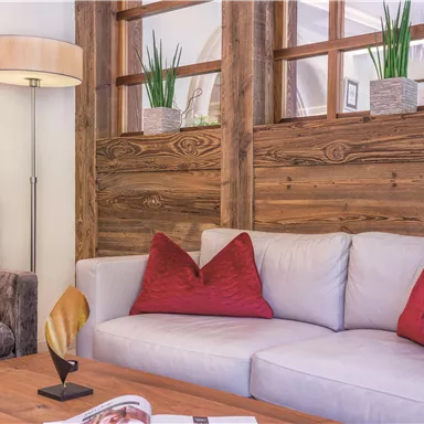 A cozy living room with a white sofa and red cushions. There is also a wooden wall and a floor lamp that creates an inviting atmosphere.