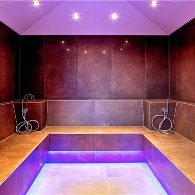 A modern wellness area with a sauna landscape and gentle purple light. The walls are made of dark material and invite relaxation.