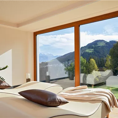 An elegant room with two loungers and large windows. The view extends over a picturesque mountain landscape.