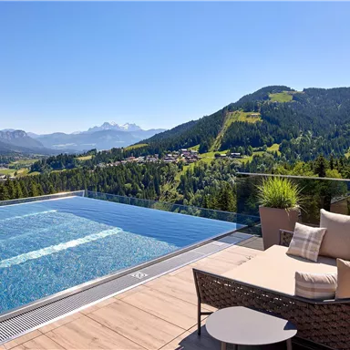 A luxurious infinity pool with a view of an impressive mountain landscape. Comfortable lounge furniture and a parasol are located next to the pool.