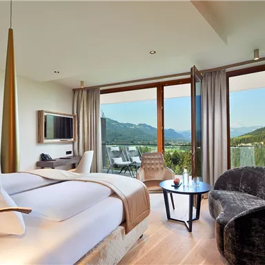 A modern hotel room with a bedroom, a television, and a splendid view of the mountains. Large windows and stylish furniture create an inviting atmosphere.