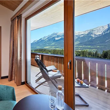 A stylish room with a view of the mountains and a balcony. The view offers a clear, sunny sky landscape.
