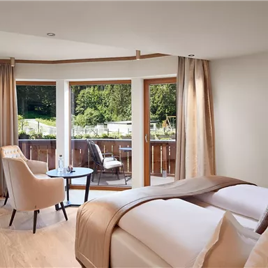 A modern room with two beds and a cozy seating area. Large windows offer a view of nature.