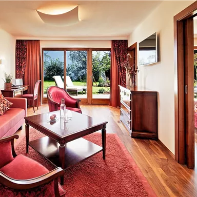 A stylish living room with a red sofa and an elegant table. Large windows provide a view of the garden.