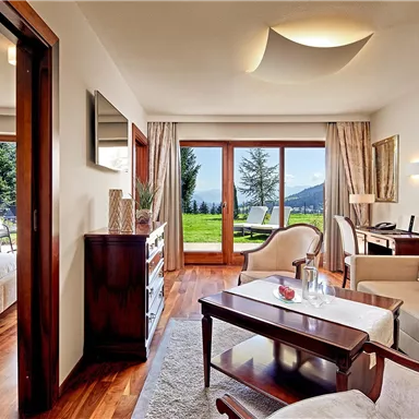 A modern room with a cozy living area and access to a beautiful balcony. In the background, there is a picturesque landscape with trees and mountains.