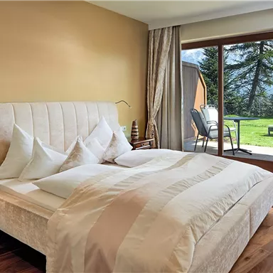 A modern bedroom with a large bed and soft colors. Large windows offer a view of the terrace and the garden.