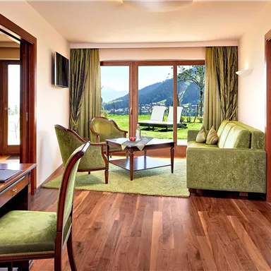 A stylish room with wooden floors and modern furniture. Large windows offer a view of the surrounding mountains and the garden.