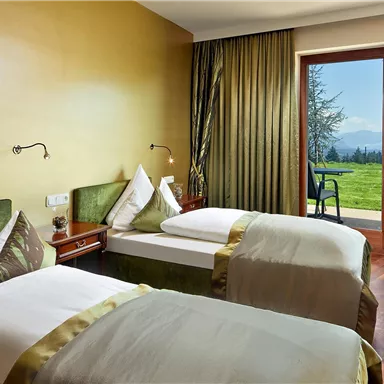 A bright hotel room with two separate beds and elegant furnishings. The large windows offer a beautiful view of the surrounding landscape and the garden.