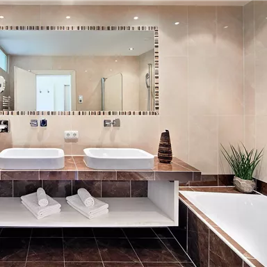 A modern bathroom with two sinks and a spacious mirror. The decor is stylish with bright tiles and a towel rack.