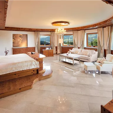 An elegant bedroom with wooden paneling and large windows. There is a cozy bed and a sitting area with modern furnishings.