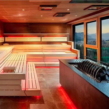 A modern wellness area with a sauna and gentle, red lights. Large windows offer a beautiful view of the landscape.