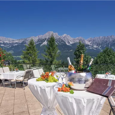 A beautiful terrace with a view of the mountains. Tables are decorated with flowers, and a champagne cooler is ready on one table.