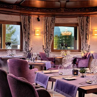 An elegant restaurant with purple chairs and tablecloths. Large windows provide a view of the surroundings.