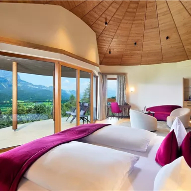 A modern room with large windows and a view of the mountains. The decor is stylish with colorful accents in pink and light wood.