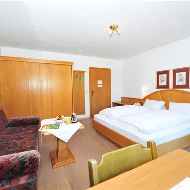 A cozy hotel room with a double bed and a seating area. There are wooden cabinets and a table with a small breakfast.