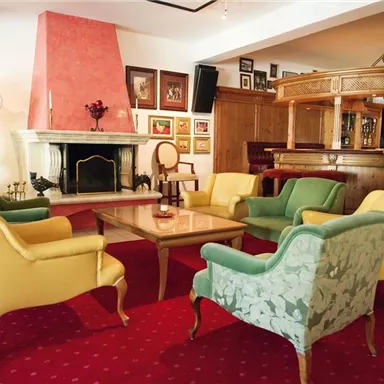 An elegant living room with a fireplace and colorful armchairs around a table. The walls are decorated with artworks, and a stylish atmosphere can be felt.