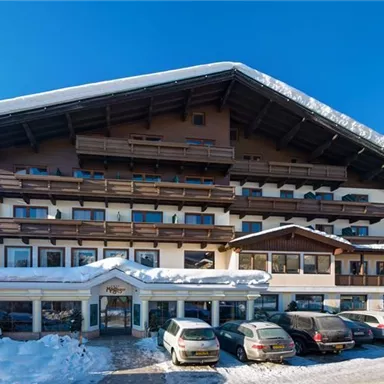 A cozy hotel in a snowy landscape. The façade is designed in traditional Alpine style and is surrounded by snow-covered mountains.