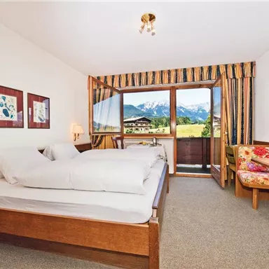 A cozy room with two beds, a table, and chairs. Through the window, a beautiful view of the mountains is visible.