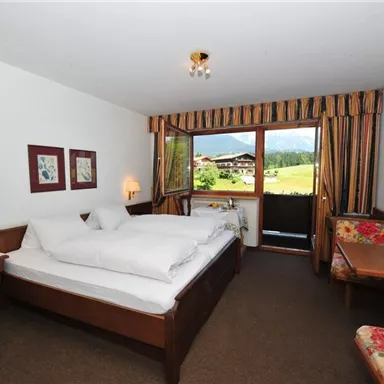 A cozy hotel room with two single beds and a wooden desk. Through the window, there is a view of the landscape.