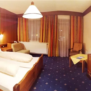 Ein gemütliches Hotelzimmer mit zwei Betten und einem Schreibtisch. Die Wände sind in warmen Farben gestaltet und es gibt einen Fernseher sowie ein Fenster mit Vorhängen.