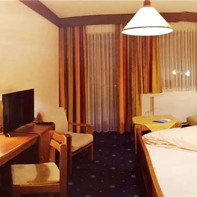 Ein gemütliches Hotelzimmer mit einem Doppelbett und einer Sitzecke. Der Raum hat warmes Licht und eine freundliche Atmosphäre.