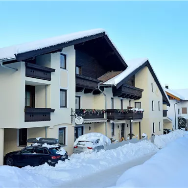 Ein schneebedecktes Wohngebäude mit zwei Etagen und Balkonen. Die Umgebung ist winterlich und ruhig.