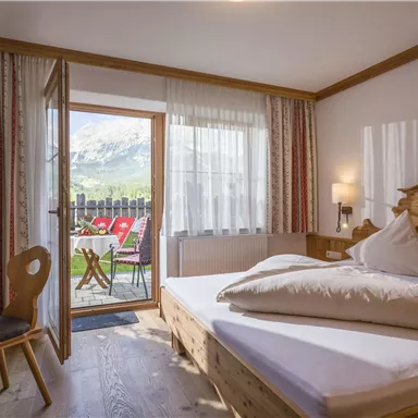 Ein gemütliches Schlafzimmer mit einem Doppelbett und Holzmobiliar. Von der Tür aus führt ein Balkon mit Blick auf die Natur.