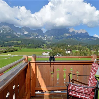 Ein Balkon mit Blick auf majestätische Berge und eine grüne Landschaft. Die Wolken sind leicht und der Himmel ist blau.