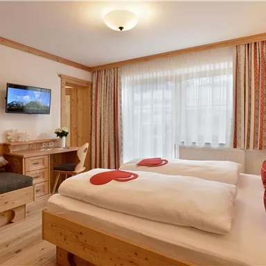 Ein gemütliches Schlafzimmer mit zwei Betten und einer Sitzgelegenheit. Große Fenster sorgen für viel Tageslicht.