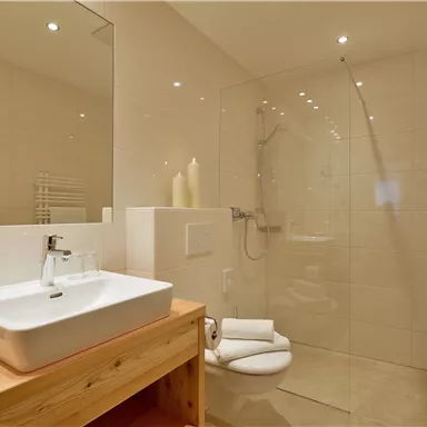 Ein modernes Badezimmer mit einer Dusche und einem Waschbecken aus Holz. Die Wände sind hell gefliest und es gibt frische Handtücher.