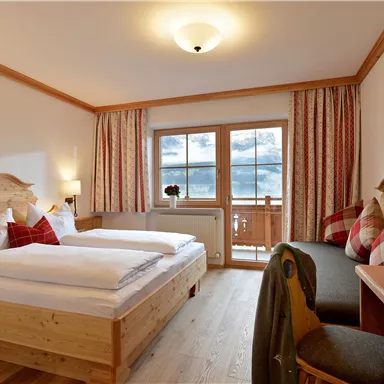 Ein gemütliches Hotelzimmer mit zwei Betten und Holzmobiliar. Große Fenster bieten einen Blick nach draußen, dekorative Kissen und Früchte auf dem Tisch sorgen für eine einladende Atmosphäre.