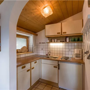 A cozy kitchen with wooden elements and bright lighting. The equipment includes a stove, a sink, and shelves with dishes.