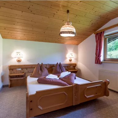 A cozy bedroom with a wooden ceiling and two beds. Large windows let in plenty of daylight and create an inviting atmosphere.