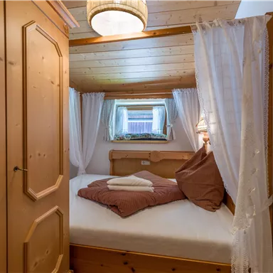 A cozy bedroom with wooden details and a large bed. The window lets in soft light, creating an inviting atmosphere.