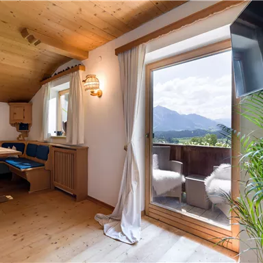 A cozy living room with a wooden ceiling and a large window front. The view extends to the mountains and a balcony.