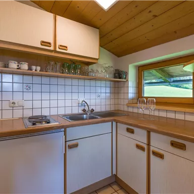 A bright kitchen with wooden shelves and modern appliances. There is a window overlooking the outside and plenty of storage space.