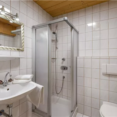 A modern bathroom with a glass shower and a sink. The walls are brightly tiled and there are wooden accents on the ceiling.
