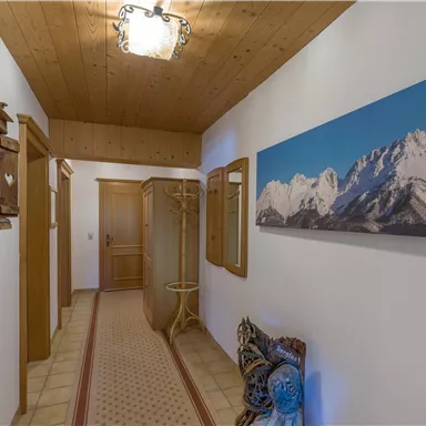 A bright hallway with wood decor and a large painting of mountains. The walls are in neutral colors and the floor is tiled.