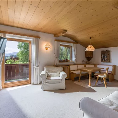 A cozy living space with a wooden floor and wooden ceiling. There is a dining table, a television, and large windows with a view outside.
