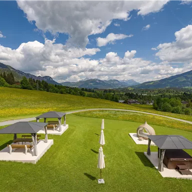 Eine schöne grüne Wiese mit mehreren Pavillons und Sonnenschirmen. Im Hintergrund sind Berge und ein klarer Himmel zu sehen.