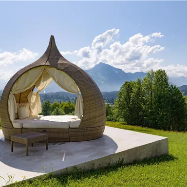 A beautiful, individual lounging area outdoors with a view of mountains and trees. The clear sky and the relaxed atmosphere invite you to unwind.