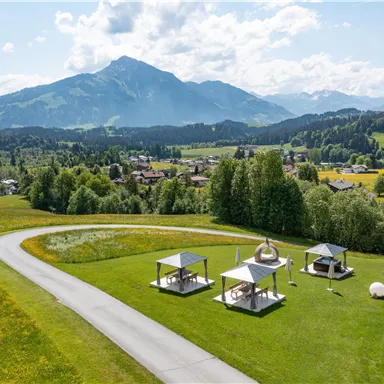Eine schöne Landschaft mit hohen Bergen im Hintergrund. Im Vordergrund befinden sich Pavillons auf einer grünen Wiese.
