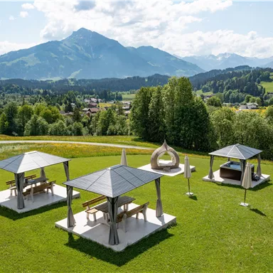 Eine großzügige Wiese mit mehreren Pavillons und Blick auf die Berge. Die Landschaft ist grün und einladend, ideal für entspannte Momente in der Natur.