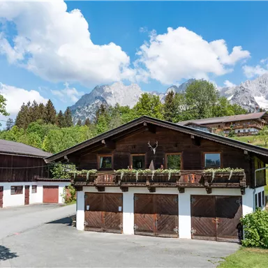 A traditional alpine house with a beautiful balcony. In the background, majestic mountains and a blue sky can be seen.
